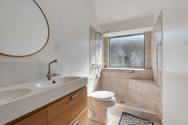 bathroom with vanity, tile patterned flooring, toilet, tiled shower, and a textured ceiling