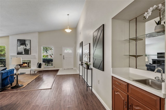 interior space with a large fireplace, vaulted ceiling, dark wood-type flooring, sink, and pendant lighting