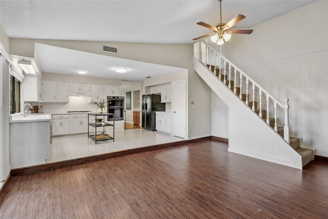 unfurnished living room with hardwood / wood-style flooring, ceiling fan, sink, and vaulted ceiling