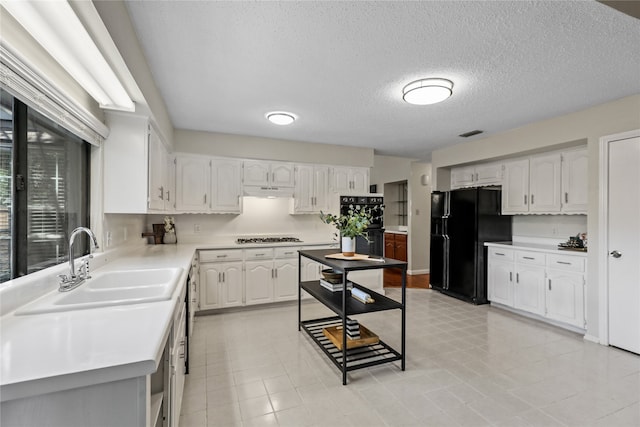 kitchen featuring sink, white cabinets, a textured ceiling, light tile patterned flooring, and black appliances