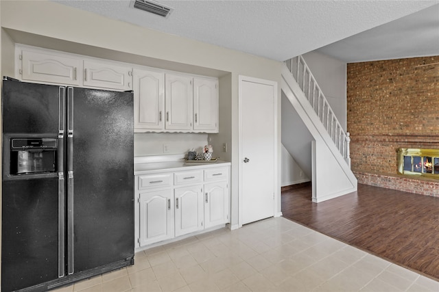 kitchen with white cabinets, a textured ceiling, light hardwood / wood-style flooring, and black refrigerator with ice dispenser