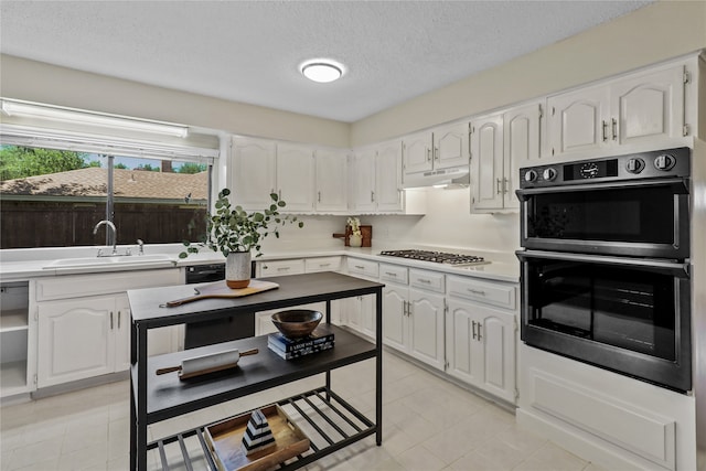 kitchen with a textured ceiling, stainless steel gas stovetop, white cabinetry, and black double oven