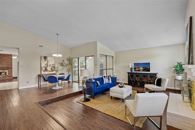 living room featuring an inviting chandelier, hardwood / wood-style flooring, a brick fireplace, and high vaulted ceiling