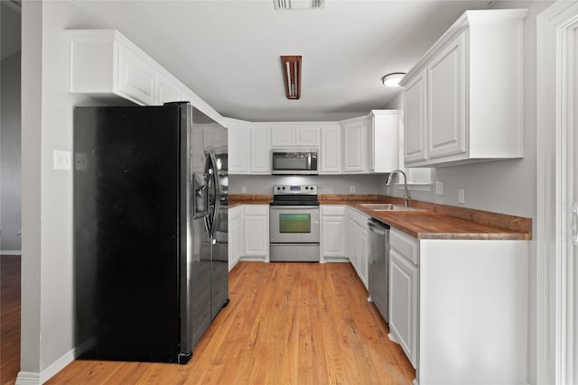 kitchen featuring butcher block counters, white cabinetry, sink, stainless steel appliances, and light hardwood / wood-style floors