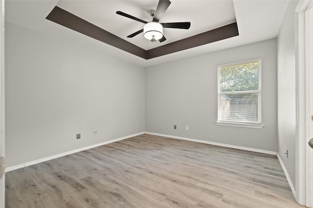 empty room with a tray ceiling, ceiling fan, and light hardwood / wood-style floors