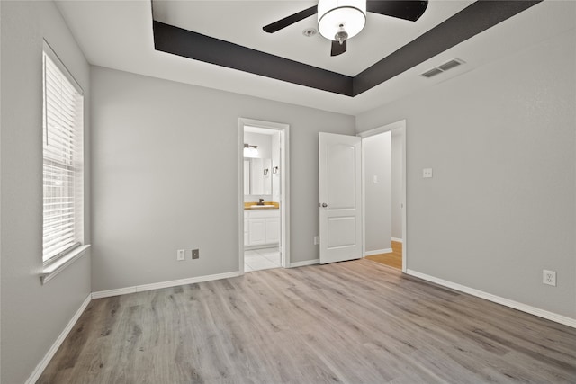 unfurnished bedroom featuring ceiling fan, light hardwood / wood-style flooring, connected bathroom, and multiple windows