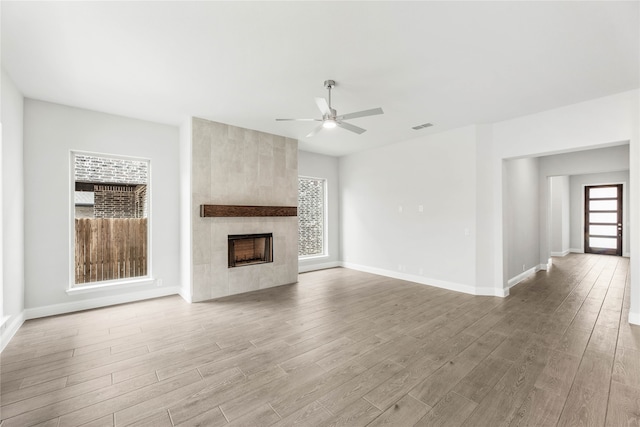 unfurnished living room featuring a large fireplace, light hardwood / wood-style flooring, a wealth of natural light, and ceiling fan