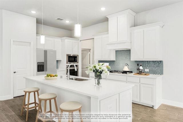 kitchen featuring white cabinetry, hanging light fixtures, stainless steel appliances, light hardwood / wood-style flooring, and a center island with sink