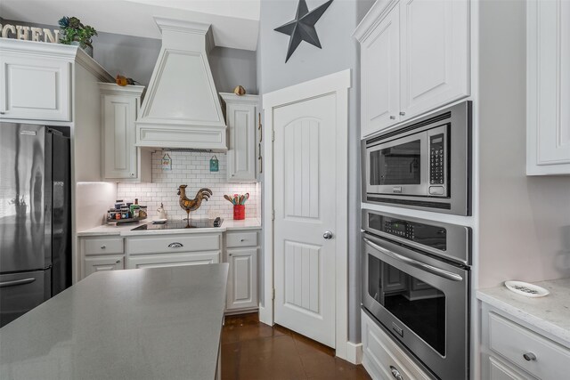 kitchen featuring stainless steel appliances, white cabinetry, custom exhaust hood, and tasteful backsplash