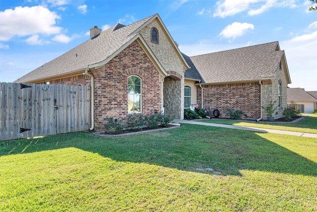 view of front of property featuring brick siding, a chimney, a front yard, fence, and stone siding