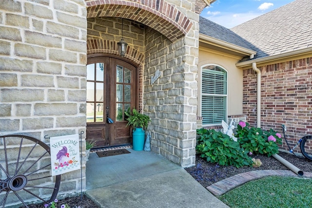 entrance to property with stone siding, french doors, a shingled roof, and brick siding