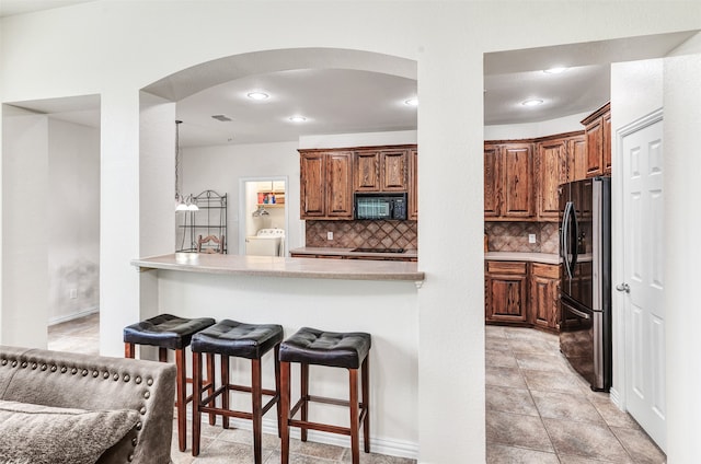 kitchen with backsplash, washer / clothes dryer, kitchen peninsula, a kitchen bar, and black appliances