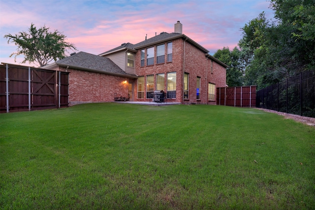 back house at dusk featuring a patio area and a yard