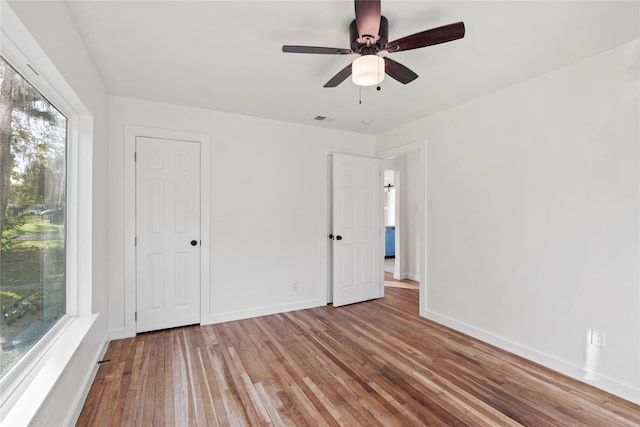 unfurnished bedroom featuring ceiling fan, wood-type flooring, and multiple windows