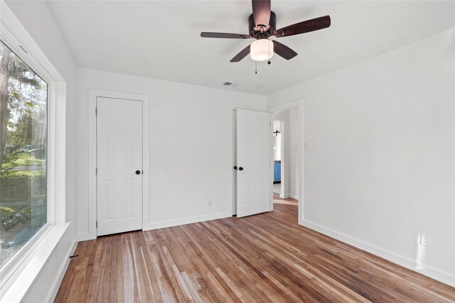 unfurnished bedroom featuring ceiling fan, wood-type flooring, and multiple windows