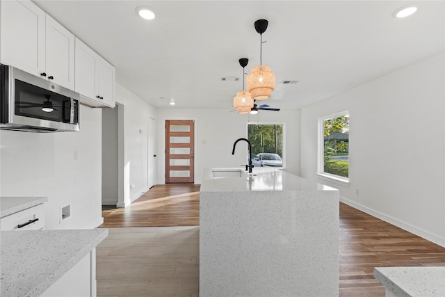 kitchen with white cabinets, light hardwood / wood-style floors, a center island with sink, and light stone countertops