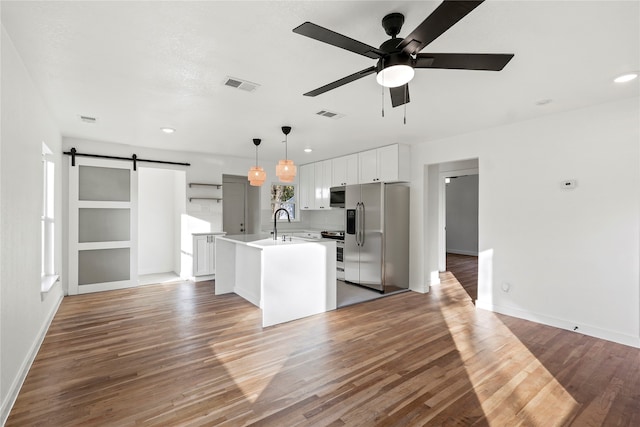 kitchen featuring wood-type flooring, a barn door, stainless steel fridge with ice dispenser, hanging light fixtures, and an island with sink