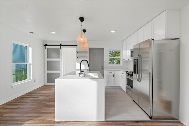 kitchen with white cabinetry, sink, a barn door, a center island with sink, and appliances with stainless steel finishes