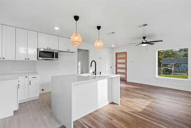 kitchen featuring hanging light fixtures, ceiling fan, an island with sink, light hardwood / wood-style floors, and white cabinetry