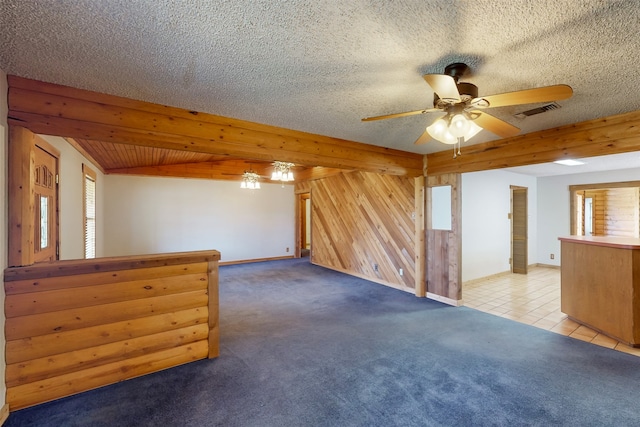 carpeted spare room with ceiling fan, wood walls, beamed ceiling, and a textured ceiling