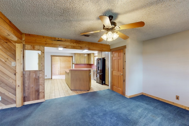 kitchen featuring wood walls, light carpet, ceiling fan, stainless steel fridge, and a textured ceiling