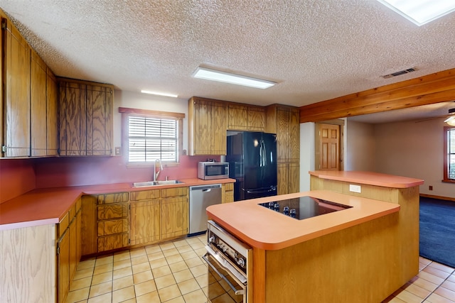 kitchen with sink, light tile patterned floors, a textured ceiling, a kitchen island, and black appliances