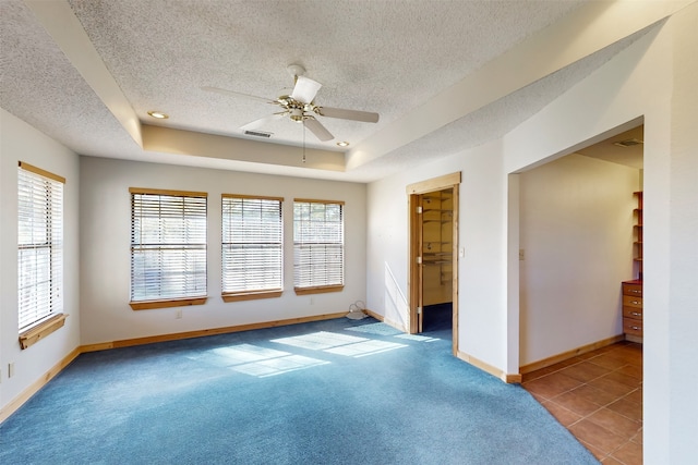 spare room featuring a textured ceiling, ceiling fan, light carpet, and a tray ceiling