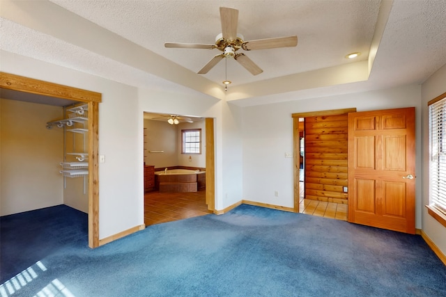 unfurnished bedroom featuring ceiling fan, dark carpet, a textured ceiling, and ensuite bath