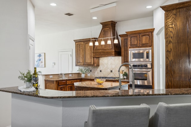 kitchen featuring kitchen peninsula, tasteful backsplash, dark stone counters, custom range hood, and stainless steel appliances