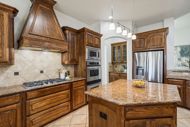 kitchen featuring a center island, backsplash, premium range hood, light stone countertops, and appliances with stainless steel finishes