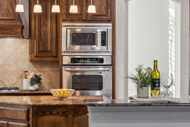 kitchen featuring hanging light fixtures, backsplash, appliances with stainless steel finishes, and dark stone counters