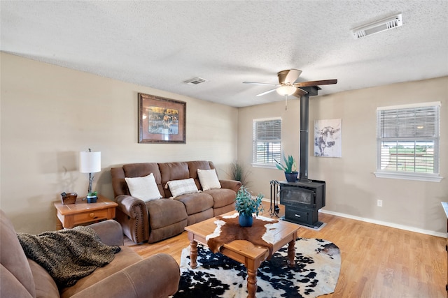 living room with a wood stove, plenty of natural light, a textured ceiling, and light hardwood / wood-style flooring