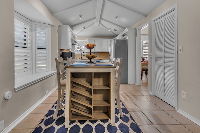 kitchen featuring white cabinetry, light tile patterned floors, vaulted ceiling with beams, and stainless steel refrigerator