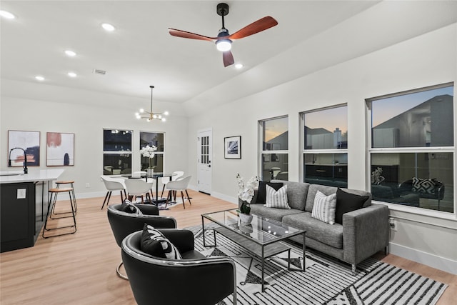 living room with ceiling fan with notable chandelier, light wood-type flooring, and sink