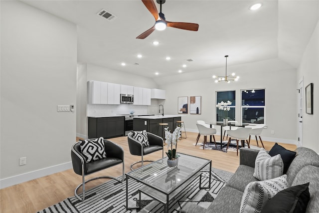 living room with light wood-type flooring, ceiling fan with notable chandelier, vaulted ceiling, and sink