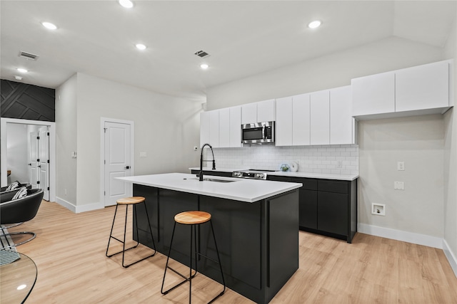 kitchen with light wood-type flooring, stainless steel appliances, a kitchen island with sink, and sink