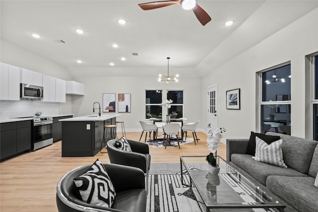 living room featuring ceiling fan with notable chandelier, sink, and light hardwood / wood-style flooring