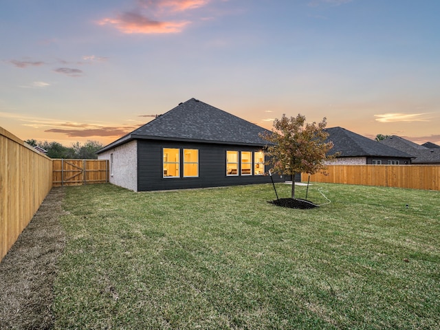 back house at dusk featuring a lawn