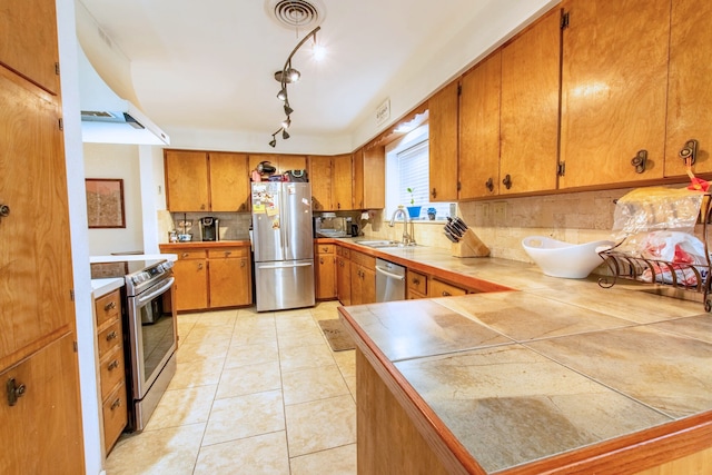 kitchen with tile counters, sink, stainless steel appliances, decorative backsplash, and exhaust hood