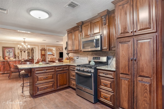 kitchen featuring kitchen peninsula, appliances with stainless steel finishes, light wood-type flooring, a kitchen breakfast bar, and an inviting chandelier