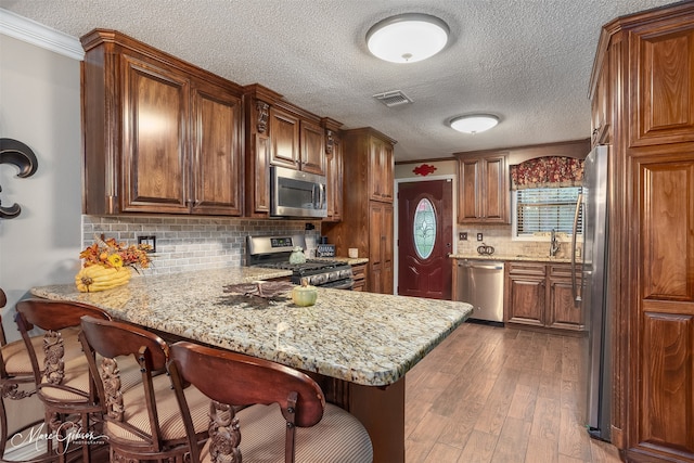 kitchen featuring kitchen peninsula, appliances with stainless steel finishes, backsplash, ornamental molding, and hardwood / wood-style flooring