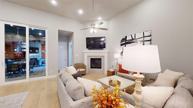 living room with ceiling fan, light wood-type flooring, and a tile fireplace