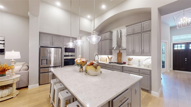 kitchen featuring pendant lighting, a kitchen island, wall chimney range hood, and appliances with stainless steel finishes