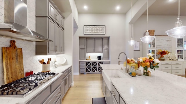 kitchen featuring light wood-type flooring, light stone counters, wall chimney exhaust hood, decorative light fixtures, and stainless steel gas stovetop