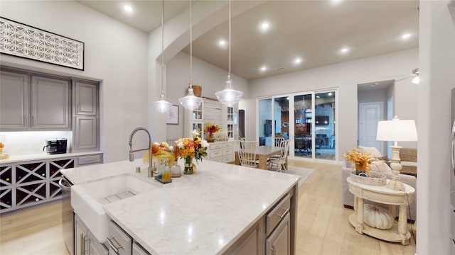 kitchen featuring light stone countertops, sink, hanging light fixtures, an island with sink, and light hardwood / wood-style floors