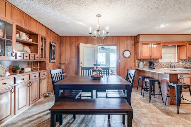 dining area featuring crown molding, a chandelier, a textured ceiling, and wood walls