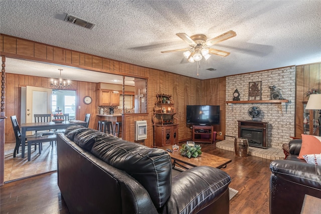 living room with ceiling fan with notable chandelier, heating unit, a fireplace, dark wood-type flooring, and a textured ceiling