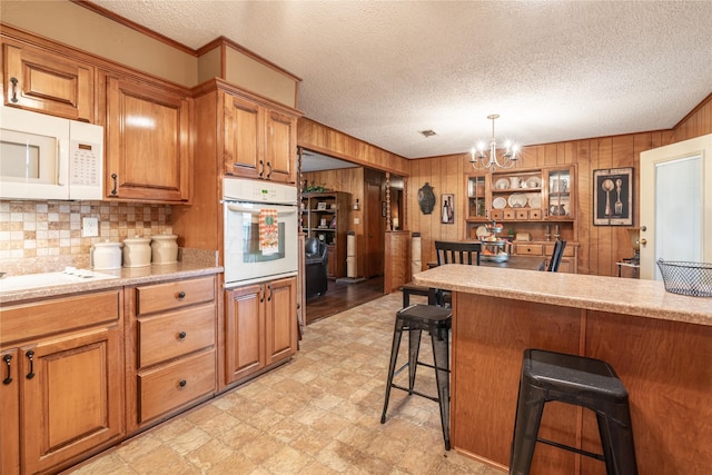 kitchen featuring a breakfast bar area, a chandelier, wooden walls, pendant lighting, and white appliances