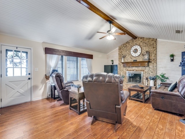 living room featuring ceiling fan, lofted ceiling with beams, light wood-type flooring, and a brick fireplace