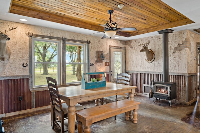 dining area featuring a raised ceiling, a wood stove, ceiling fan, and wooden ceiling